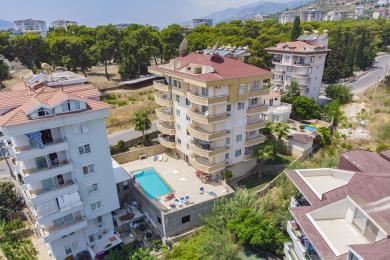 Σύγχρονο διαμέρισμα σε συγκρότημα στην Αλάνια με θέα στο βουνό, μοντέρνα αρχιτεκτονική και ζεστή, ηλιόλουστη ατμόσφαιρα.